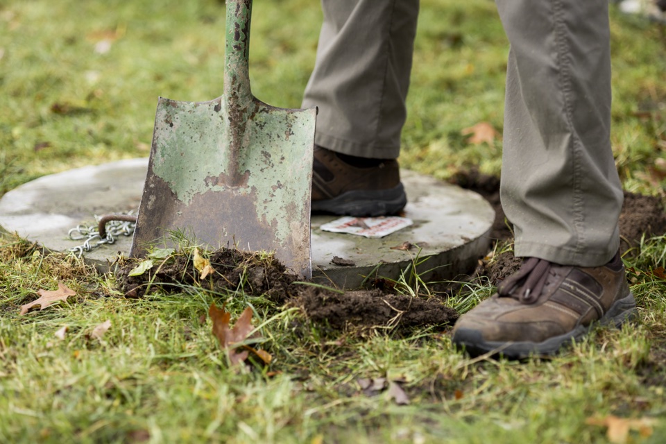 Inspector using a shovel to clear soil around a septic cover